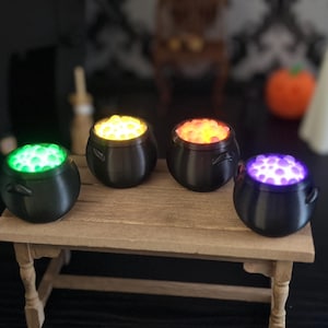 A slightly angled close-up view of the four miniature bubbling cauldrons on the wooden table, with Halloween props blurred in the background.