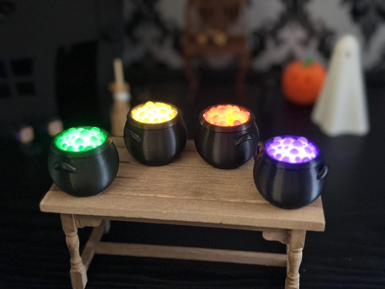 A slightly angled close-up view of the four miniature bubbling cauldrons on the wooden table, with Halloween props blurred in the background.