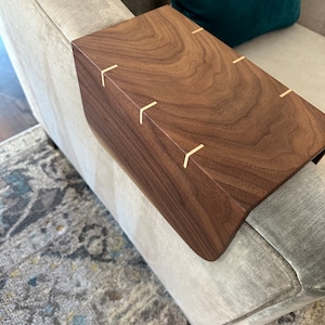 May include: A wooden armrest tray with a dark brown walnut finish. The tray has a curved edge and is decorated with small brass accents.