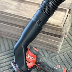 May include: A red and black Milwaukee FUEL power sander with a black dust collection hose attached. The sander has a textured grip and a red trigger.