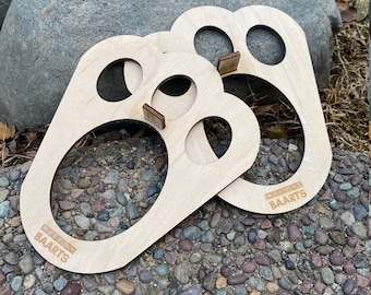 Op de afbeelding: Twee houten ringwerpspelstukken met de tekst "MADE BY BAARTS" op elk stuk. De stukken liggen op een bed van kleine, kleurrijke stenen.