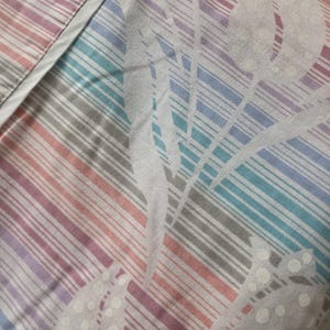 May include: A fabric textile featuring a pattern of vertical stripes in shades of pink, purple, blue, and gray. Overlaid on the stripes is a subtle, tone-on-tone floral design with dotted textures, creating a layered visual effect across the material.