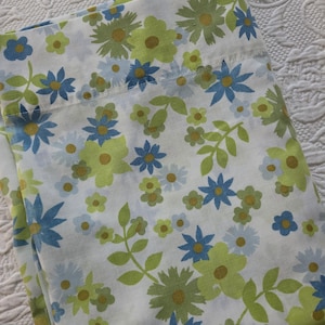 May include: A white fabric sheet featuring a repeating floral pattern with various sizes of flowers in shades of lime green, light blue, and dark blue, accented with small yellow centers and green leaves on thin stems.