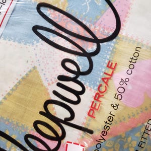 May include: A packaged percale sheet set with a patchwork pattern in pastel colors. The design includes squares of yellow, pink, and blue with floral and geometric details. The packaging reads "Percale" and "50% polyester & 50% cotton".