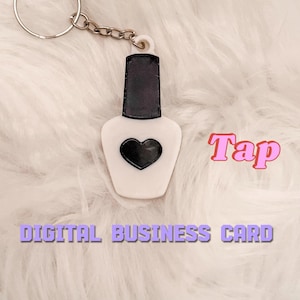 May include: A white nail polish bottle-shaped keychain with a black heart and a black cap. The keychain has a silver chain and ring. Text on the image reads "Tap" and "DIGITAL BUSINESS CARD".