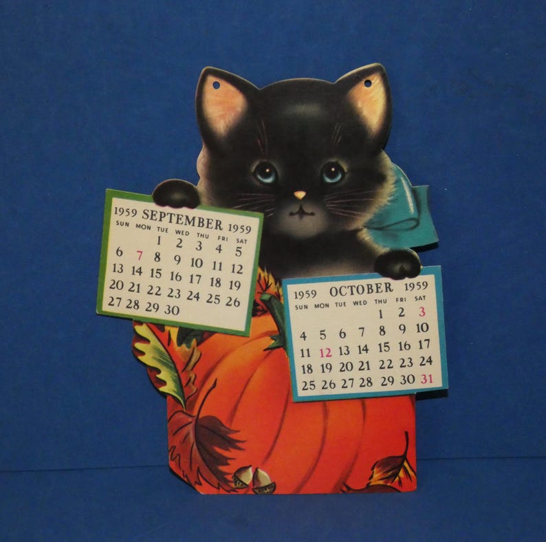May include: A vintage 1959 wall calendar featuring a black kitten with blue eyes and a blue bow, holding two paper calendar sheets for September and October 1959. The kitten is positioned behind a large orange pumpkin with autumn leaves and acorns.