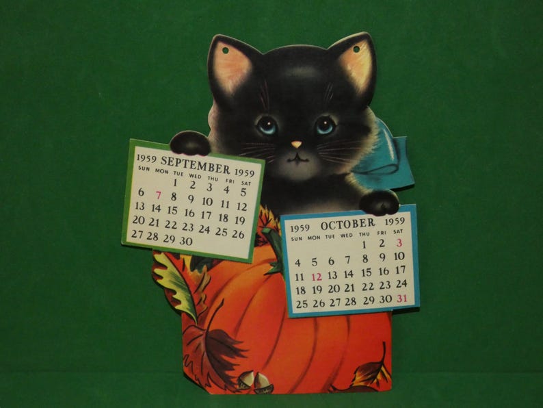 May include: A vintage 1959 wall calendar featuring a black kitten with blue eyes peeking over a large orange pumpkin. The kitten holds two paper calendar pages for September and October 1959. The design includes autumn leaves and acorns.