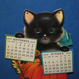 May include: A vintage 1959 calendar featuring a black kitten with blue eyes and a teal bow, holding two paper calendar pages for September and October 1959. The kitten is positioned in front of a large orange pumpkin with green leaves.