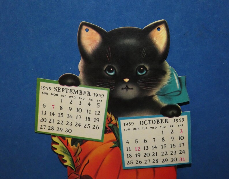 May include: A vintage 1959 calendar featuring a black kitten with blue eyes and a teal bow, holding two paper calendar pages for September and October 1959. The kitten is positioned in front of a large orange pumpkin with green leaves.