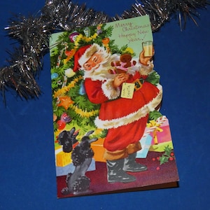 May include: Vintage Christmas card featuring Santa Claus in a red suit, holding a drink and a teddy bear, with two black poodles looking up at him. The card has a Christmas tree and the text "Merry Christmas Happy New Year!"