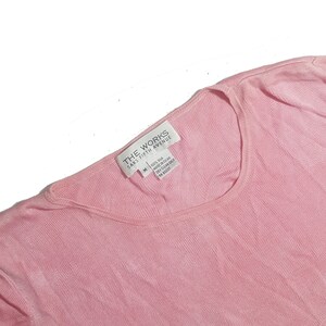 May include: A pink, short-sleeved, ribbed knit top with a white tag that reads "THE WORKS SAKS FIFTH AVENUE" and "100% Silk Made in China Dry Clean Only M (US) 00237"