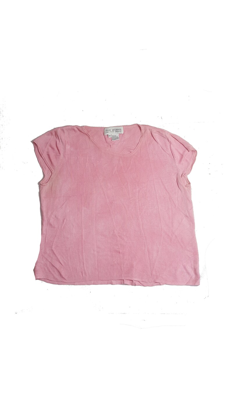 May include: A pink short-sleeved knit top with a scoop neck. The label reads "The Works Easy Fit Apparel".