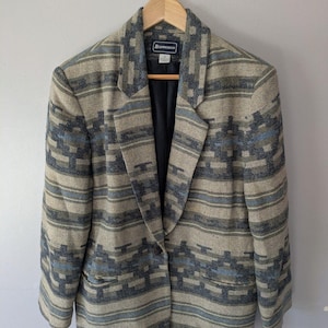 May include: A blazer featuring a woven pattern in shades of tan, dark blue, and light blue. The garment has a notched lapel, a single button closure, and two front pockets. The interior is lined with black fabric and includes a Requirements brand label.