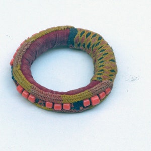 May include: A red, green and black fabric bracelet with a row of pink beads.