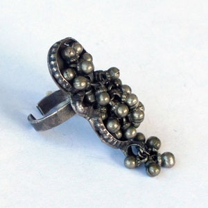 Puede incluir: Un anillo de plata con un racimo de pequeñas cuentas que cuelgan de la banda. El anillo es abierto y ajustable.
