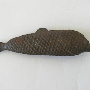 Puede incluir: Una detallada escultura de pez de color bronce con un patrón texturizado en forma de escamas. El pez tiene una aleta dorsal prominente y una cola bifurcada. La escultura es probablemente de metal y tiene un aspecto envejecido.