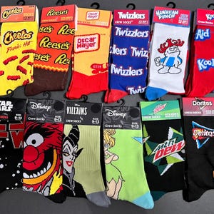May include: A collection of 10 pairs of crew socks featuring various popular brands and logos, including Cheetos, Reese's, Oscar Mayer, Twizzlers, Hawaiian Punch, Kool-Aid, Star Wars, Disney, Villains, and Doritos. The socks are all black, white, red, blue, green, and yellow.