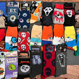 May include: A collection of colorful socks featuring various pop culture characters and designs.  The socks include characters from E.T.,  Friday the 13th,  Happy Gilmore,  Rugrats,  and more.  The socks are all new and have the words "Socks" printed on the packaging.