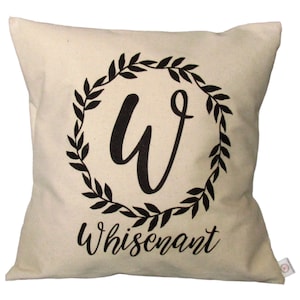 Op de afbeelding: Een crèmekleurig kussen met een zwart kransontwerp met de letter "W" en de naam "Whisenant".