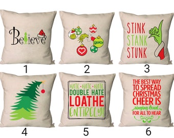 Puede incluir: Seis diseños diferentes de almohadas con el Grinch de la película ¡Cómo el Grinch robó la Navidad!. Las almohadas son de color beige con texto e imágenes verdes y rojas. El texto en las almohadas incluye "Believe", "Stink Stank Stunk", "Hate Hate Hate Double Hate Loathe Entirely", y "The Best Way to Spread Christmas Cheer is Singing Loud for All to Hear".