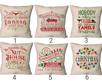 Puede incluir: Seis diseños diferentes de almohadas de temática navideña. Las almohadas son todas blancas con acentos rojos, verdes y dorados. Los diseños incluyen un servicio de entrega de árboles de Navidad, una Navidad familiar, una casa de nueces, una Navidad familiar Griswold, una feliz Navidad y un ponche de huevo navideño.
