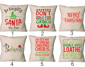 Puede incluir: Seis diseños de cojín diferentes con temática navideña. Los cojines son todos blancos con texto y gráficos verdes y rojos. Los diseños incluyen "Be Naughty save SANTA the trip", "DON'T be a GRINCH", "MERRY CHRISTMAS", "Believe", "The best way to spread Christmas cheer is singing loud for all to hear", y "Hate Hate Hate Double Hate Loathe Entirely!"