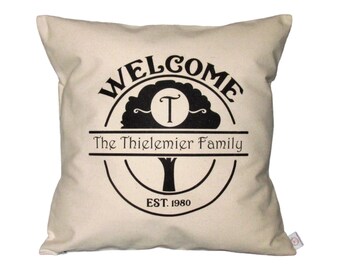May include: A white throw pillow with a black design of a tree with a circle around it. The text "WELCOME" is above the tree and "The Thielemier Family EST. 1980" is below the tree.