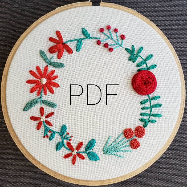 以下が含まれることがあります： 白い刺繍枠に、花輪のデザインが施されています。花輪は赤と緑の花と葉でできています。枠の中央には黒い文字で「PDF」と書かれています。