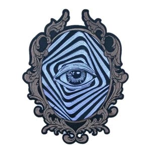 May include: An embroidered patch featuring an eye within a distorted, striped pattern, framed by an ornate, brown and black border. The eye is detailed with a light blue iris and black pupil, creating a surreal, artistic design.
