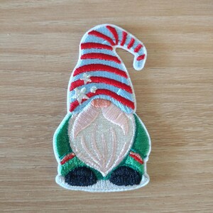 May include: Embroidered gnome patch with a blue and red striped hat, white beard, and green jacket. The patch features a whimsical design with star accents on the hat, perfect for adding a festive touch to clothing or accessories.