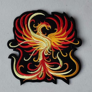 May include: Embroidered iron-on patch featuring a red, yellow, and white phoenix rising from flames against a black background.