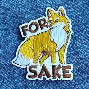 May include: Embroidered patch featuring a stylized fox in shades of yellow, brown, and white. The patch includes the text "FOR SAKE" in brown letters, outlined in white. The patch is set against a blue denim background.