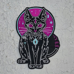 May include: Black cat patch with a mystical design. The cat is black with white outlines, pink eyes, and a blue pendant. It is set against a purple and blue background with stars. The patch is likely for clothing or accessories.