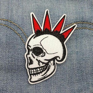 May include: Embroidered patch featuring a white skull with a black grin and eye sockets. The skull has a red and black mohawk. The patch is on a blue denim background.