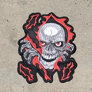 May include: A black and red embroidered patch featuring a skull with glowing red eyes, appearing to break through a black and red background.