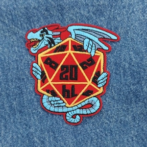 May include: A blue and red embroidered patch of a dragon holding a red twenty-sided die. The die has black numbers and a yellow outline.