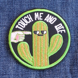 May include: Embroidered patch featuring a cartoon cactus wearing sunglasses with the text "TOUCH ME AND DIE" in white. The cactus is green and tan, with a pointing hand. The patch has a black background and a green border.