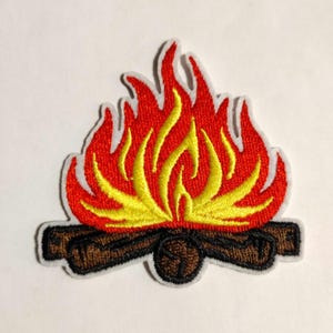 May include: Embroidered patch featuring a campfire design. The flames are red and yellow, with a white border. The logs are brown. This patch is suitable for jackets, backpacks, or other fabric items.