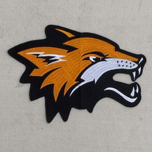 May include: An embroidered patch of a snarling fox head with orange fur, white teeth, and black and white details. The patch is on a white background.
