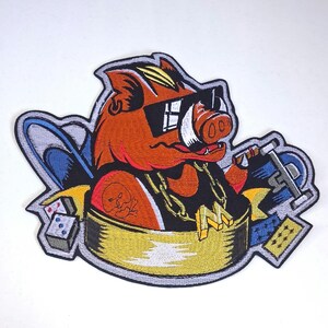May include: An embroidered patch featuring an orange boar wearing black sunglasses and a gold chain with a letter M pendant. The boar is inside a gold tub, holding a cigar, with a skull tattoo, dice, and playing cards in the background.