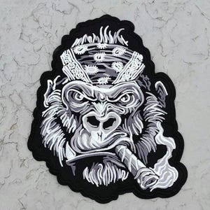 May include: Black and white embroidered patch of a gorilla wearing a bandana and smoking a cigarette.