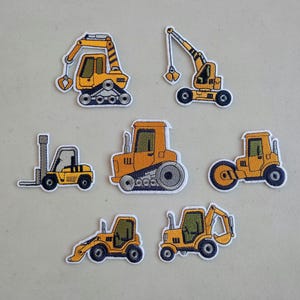 May include: A collection of seven embroidered patches featuring various construction vehicles. The patches are primarily yellow and orange, with black and white accents. The designs include a forklift, excavator, crane, and bulldozer.