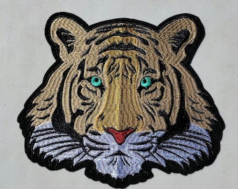 May include: Embroidered patch of a tiger's face with a black outline, brown and gold fur, and bright turquoise eyes.