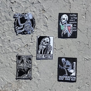 May include: A set of ten black and white embroidered iron-on patches featuring various skeleton designs with humorous sayings. The patches include "Dead Drunk", "Coffee is the only reason I'm still alive", "Stay Positive", and "Inspiration don't come easy".