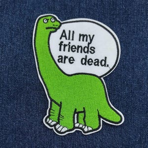 May include: Green embroidered iron-on patch of a cartoon dinosaur with a speech bubble that says "All my friends are dead."