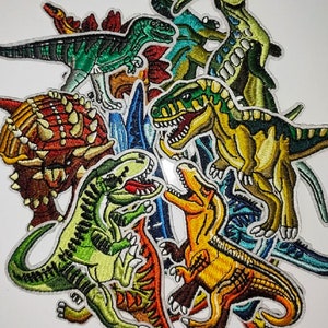 May include: A collection of colorful embroidered iron-on patches featuring various dinosaurs, including a green Tyrannosaurus Rex, a red Triceratops, and a yellow Stegosaurus.