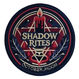 May include: A circular embroidered patch featuring a dark red background with a black candle, two black birds, and a white star outline. The text SHADOW RITES is centered in white, with OCTOBER MOON written in white along the bottom edge of the border.