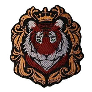 May include: An embroidered patch featuring a tiger head with green eyes, centered within a decorative gold-colored filigree frame topped with a crown. The tiger has red, white, and black fur details, all set against a solid black background.