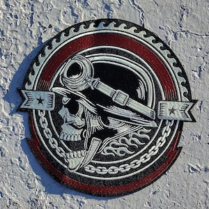 May include: A black and white embroidered patch with a skull wearing a helmet and goggles. The patch is surrounded by a red and white chain link design.