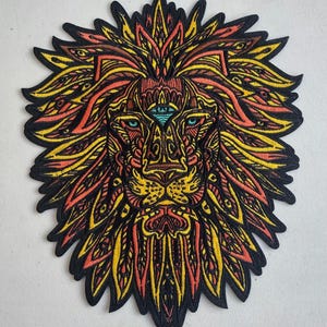 May include: A colorful embroidered patch of a lion's head with a third eye in the center of its forehead. The lion's mane is made up of intricate patterns in shades of yellow, orange, and red.